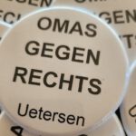 Das Foto zeigt den Ausschnitt eines Haufens von sechs Buttons zum Anstecken mit weißem Hintergrund und schwarzer Druck-Schrift. In der Mitte des Bildes ist ein Button komplett unverdeckt zu sehen. Auf ihm wie auf allen anderen steht in Großbuchstaben OMAS GEGEN RECHTS in drei Zeilen und darunter in Normalschrift Uetersen.