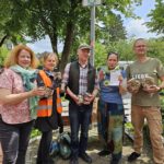 Das Foto zeigt eine Gruppe von fünf Menschen. Sie stehen neben einander und sehen alle freundlich bestimmt und ie Kamera. In den Händen halten sie Schraubverschlussgläser, gefüllt mit den gesammelten Zigarettenkippen. Im Hintergrund sieht man grüne Bäume, Büsche und den blauen Himmel mit ein paar weißen Wolken.