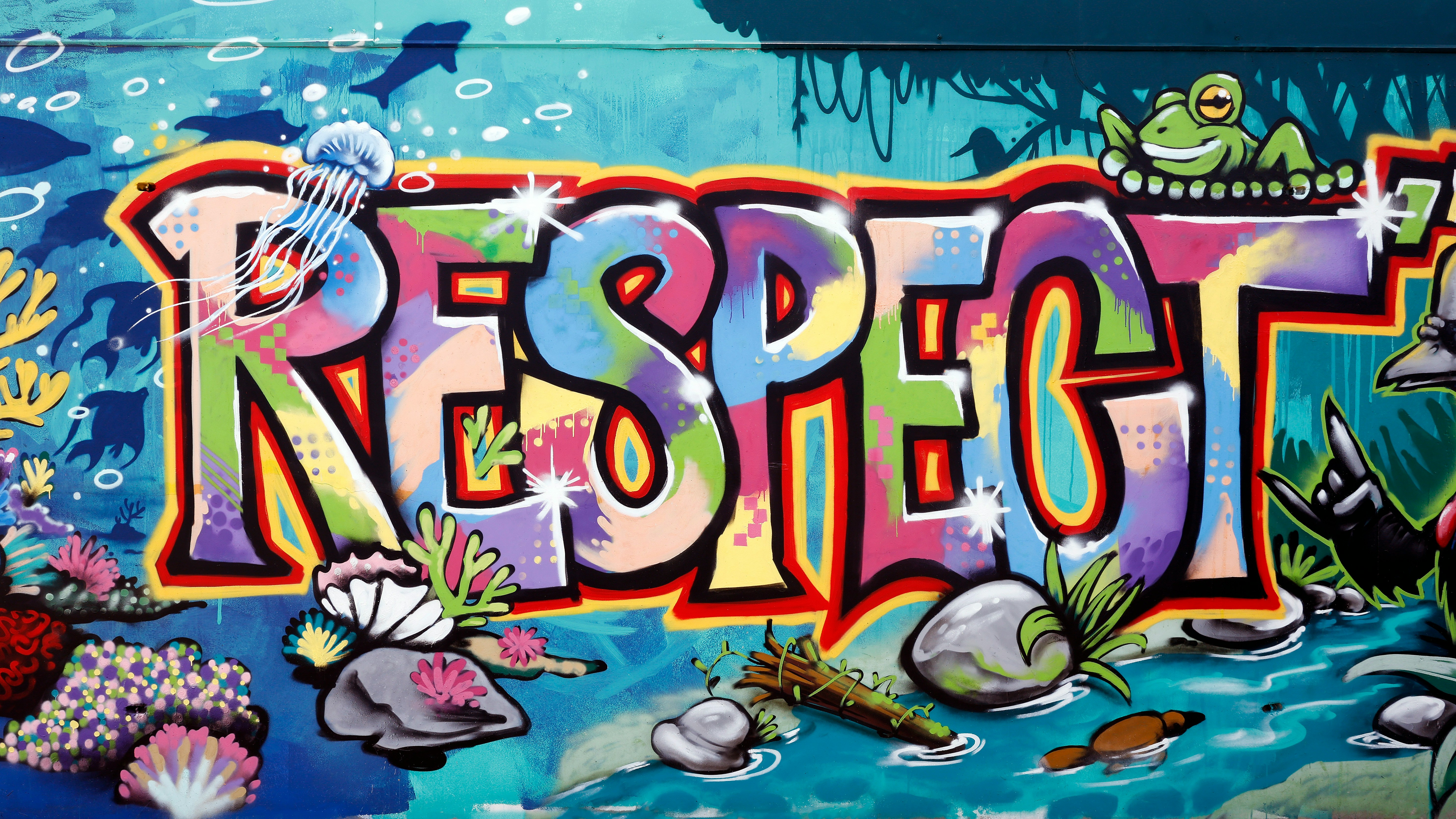 Das Foto zeigt ein Graffito mit dem großen Schriftzug RESPECT in Großbuchstaben, in bunten Farben mit schwarzer Umrandung vor dem Hintergrund einer Unterwassermeeresszenerie mit Anemonen, Muscheln, Korallen und ein paar Fischen