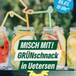 Auf dem Bild sieht man von vorn vier durchsichtige Gläser mit Fruchtscheiben, zum Beispiel von Wassermelone, Apfel, Organe, die auf einer Tischplatte stehen. In den Gläsern stecken farbige Trinkhalme. Im Hintergrund sind verschwommen grüne Büsche zu erkennen.