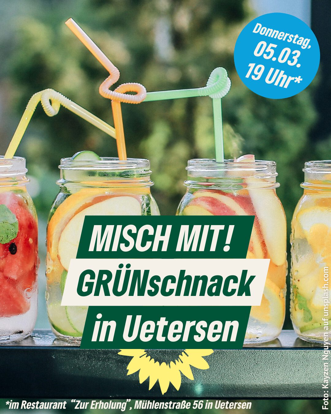 Auf dem Bild sieht man von vorn vier durchsichtige Gläser mit Fruchtscheiben, zum Beispiel von Wassermelone, Apfel, Organe, die auf einer Tischplatte stehen. In den Gläsern stecken farbige Trinkhalme. Im Hintergrund sind verschwommen grüne Büsche zu erkennen.